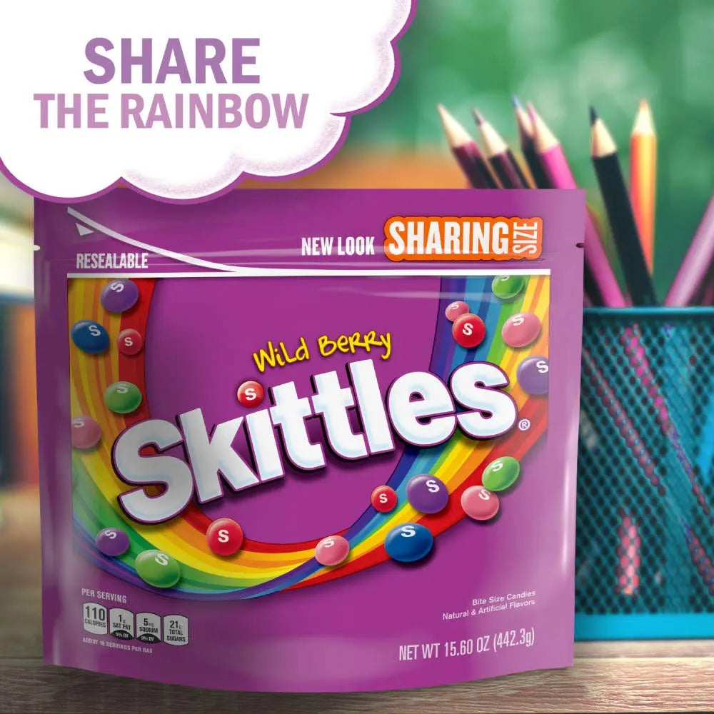 Purple Skittles package with colorful candies and 'Share the Rainbow' text, set against a blurred classroom background.